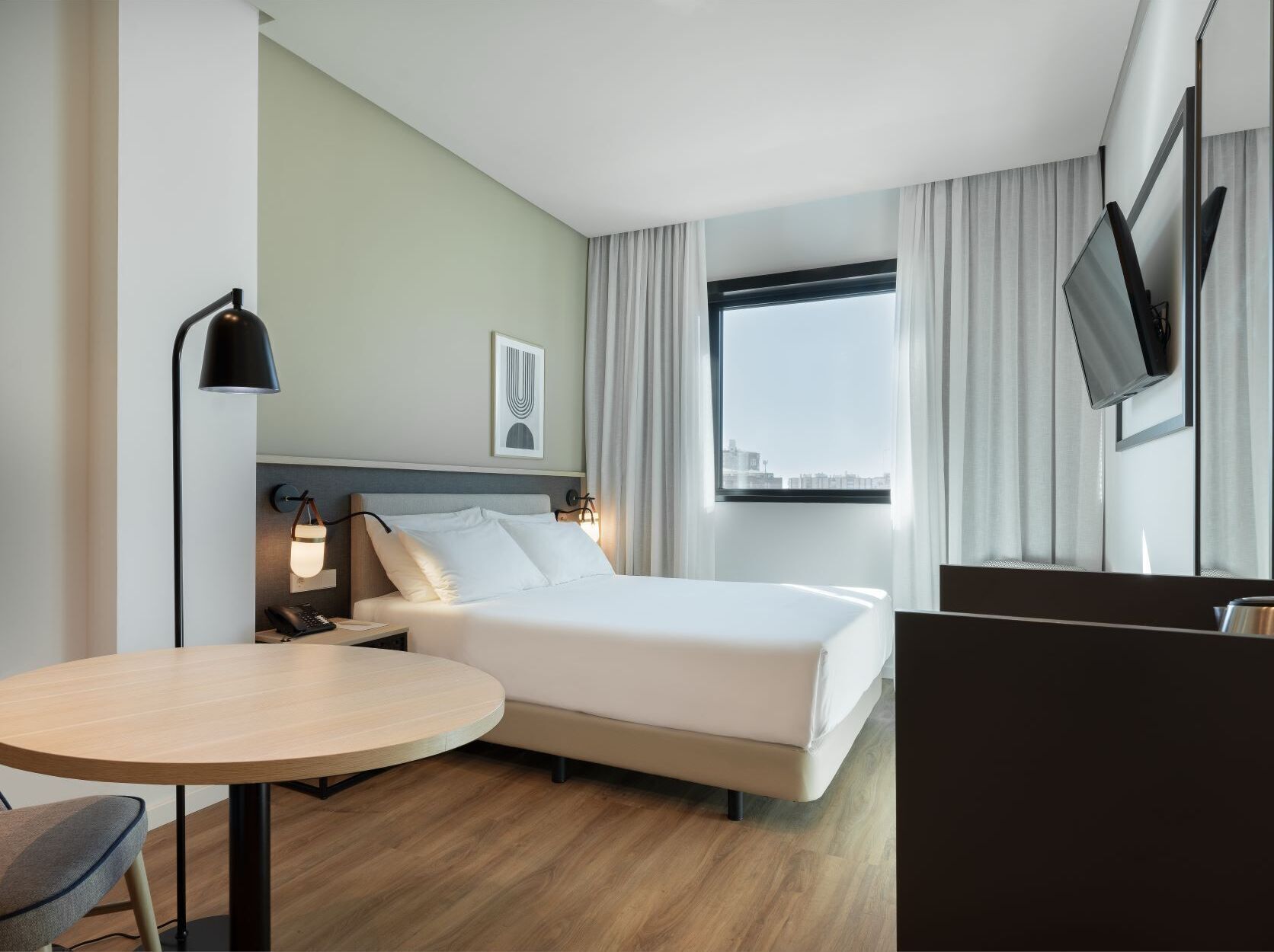A hotel room with a bed, a desk, a chair, a TV, and a window with curtains.