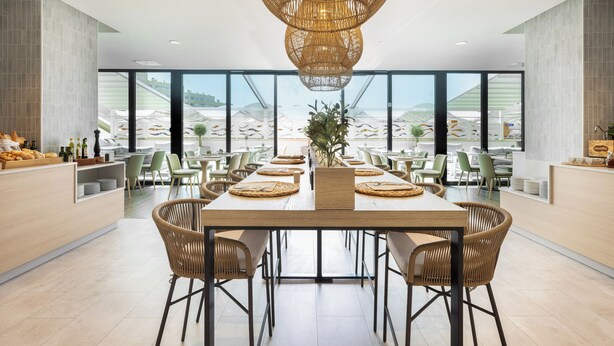 Un espace de salle à manger moderne avec une longue table, des chaises en osier et un luminaire suspendu au centre.