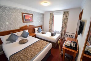 A hotel room with two beds, a desk, a chair, a television, and a window with curtains. - Pembridge Palace Hotel (London)