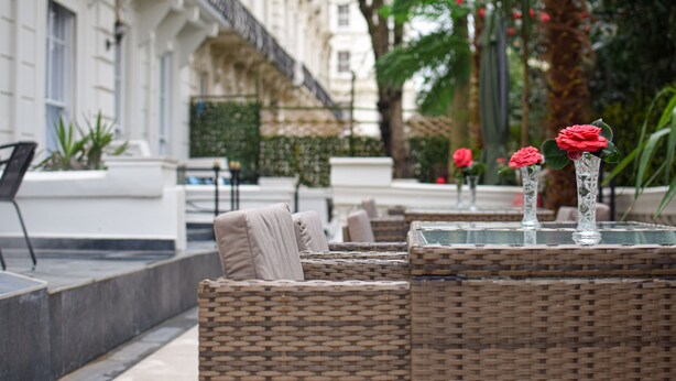 A wicker outdoor seating area with a glass table and red roses. - Pembridge Palace Hotel (London)
