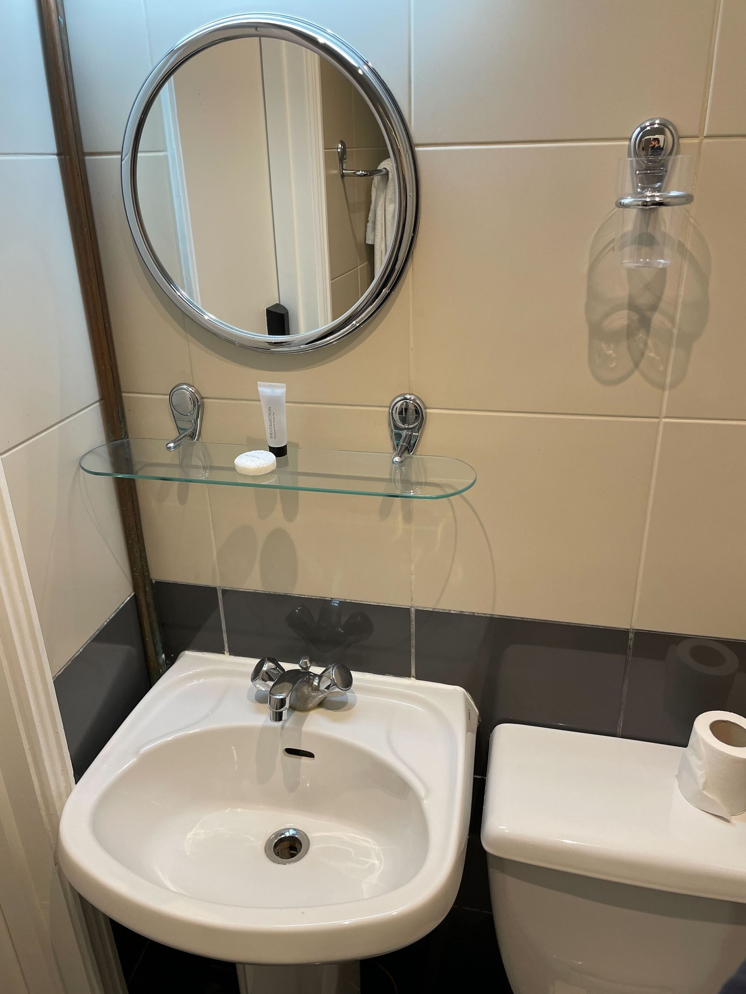 Ein Badezimmer mit Waschbecken, Glasablage, rundem Spiegel und Toilette.
