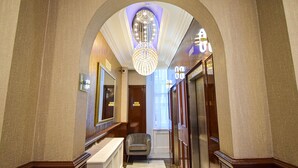 A hallway with an arched ceiling, a chandelier, a mirror, and a door. - Pembridge Palace Hotel (London)