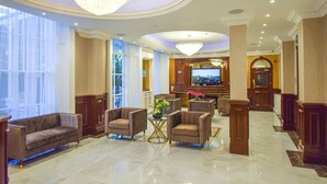 A spacious lobby with a chandelier, comfortable seating, a television, and a view of the outdoors. - Pembridge Palace Hotel (London)