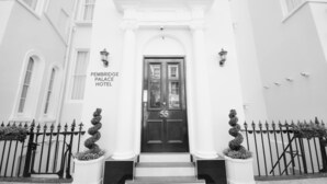 The entrance to Pembridge Palace Hotel, featuring a black double door with the number 55, white columns, and a symmetrical iron fence with topiary plants. - Pembridge Palace Hotel (London)