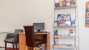 A workspace with a desk, two chairs, a computer, and a bookshelf with magazines and books. - Brunel Hotel (London)