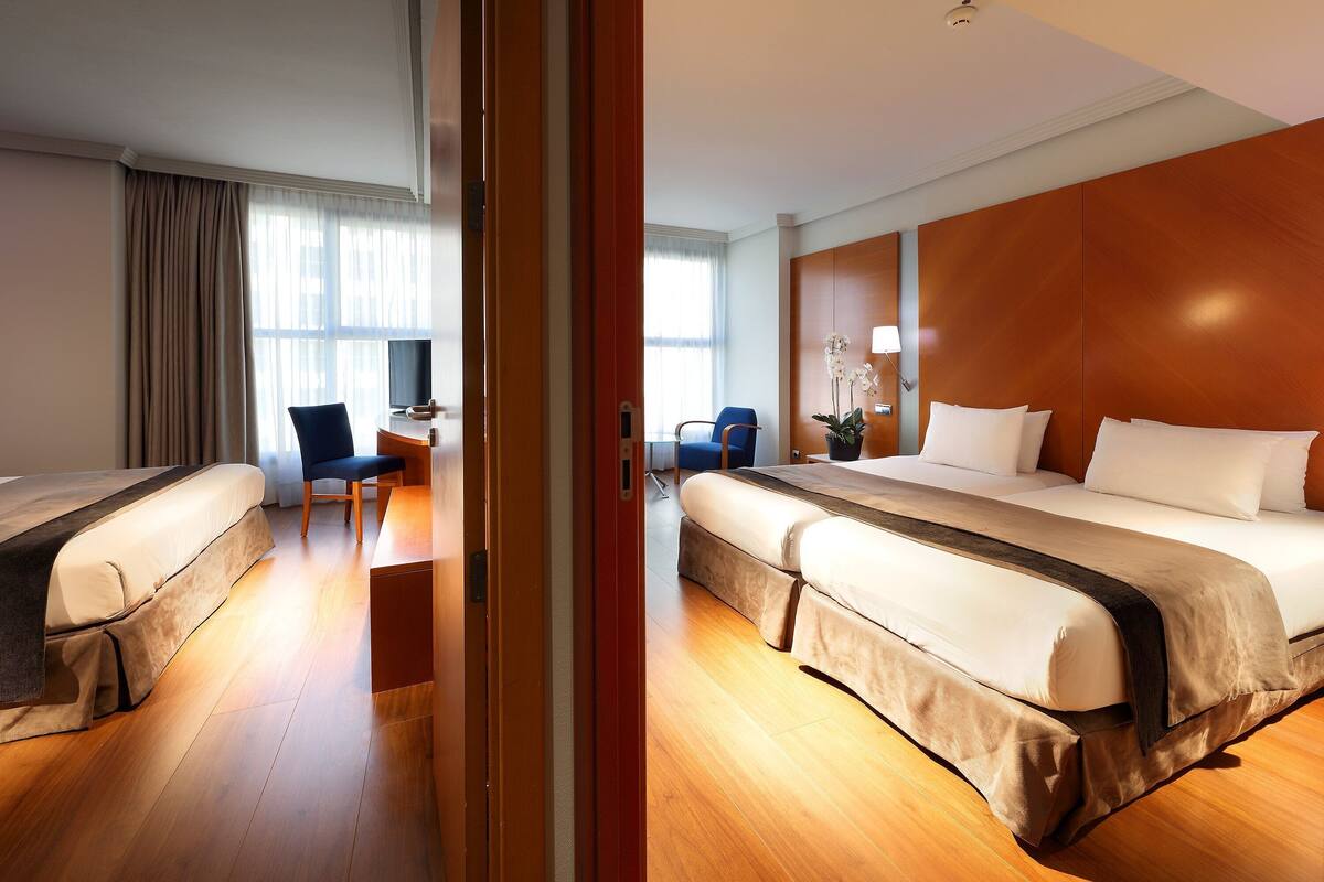 A hotel room with two beds, a desk, a chair, and a potted plant.