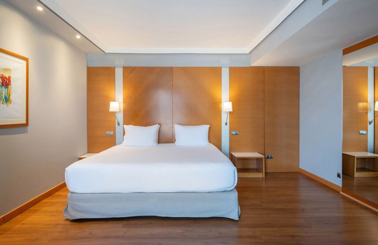 Een moderne hotelkamer met een groot bed, houten paneelwanden en twee nachtkastjes met lampen.
