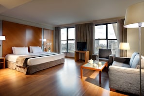 Habitación de hotel con una cama grande, un sofá, una mesa de centro, un televisor y vistas a la ciudad.