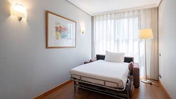 Habitación de hotel con cama, mesitas de noche, lámpara, un cuadro y una ventana con cortinas.