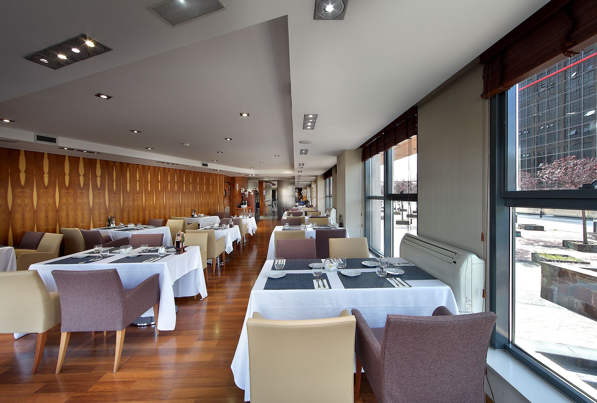 Un restaurante con varias mesas y sillas, una pared de madera y ventanas amplias.