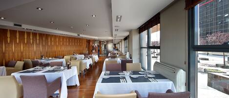 Un restaurante con varias mesas y sillas, una pared de madera y ventanas amplias.