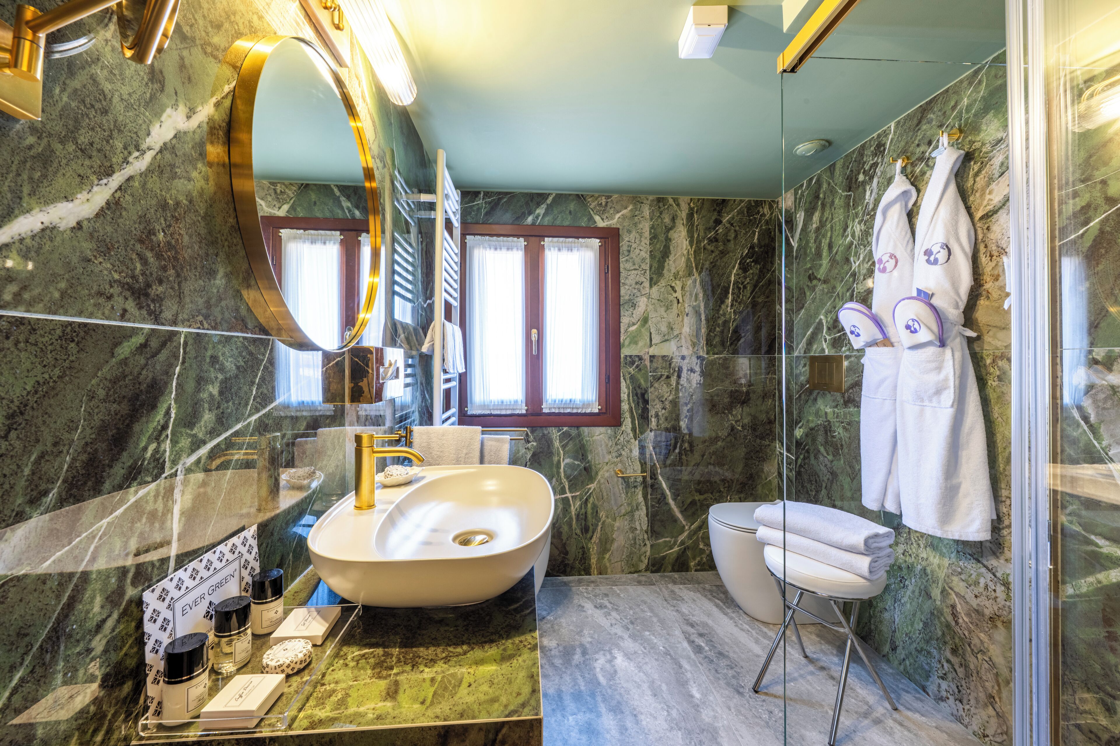 A modern bathroom with a large oval sink, a glass-enclosed shower, and marble walls.