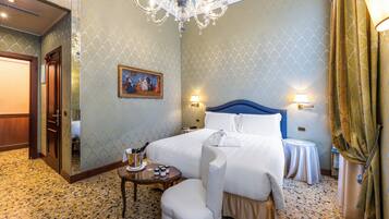Habitación de hotel con cama, una mesita con una botella de champán, una silla y un cuadro en la pared.
