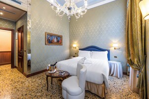 A hotel room with a bed, a small table with a bottle of champagne, a chair, and a painting on the wall.