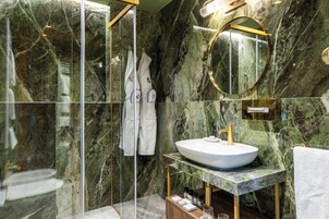 Un bagno moderno con parete in marmo, uno specchio rotondo, un lavabo bianco e cabina doccia in vetro.