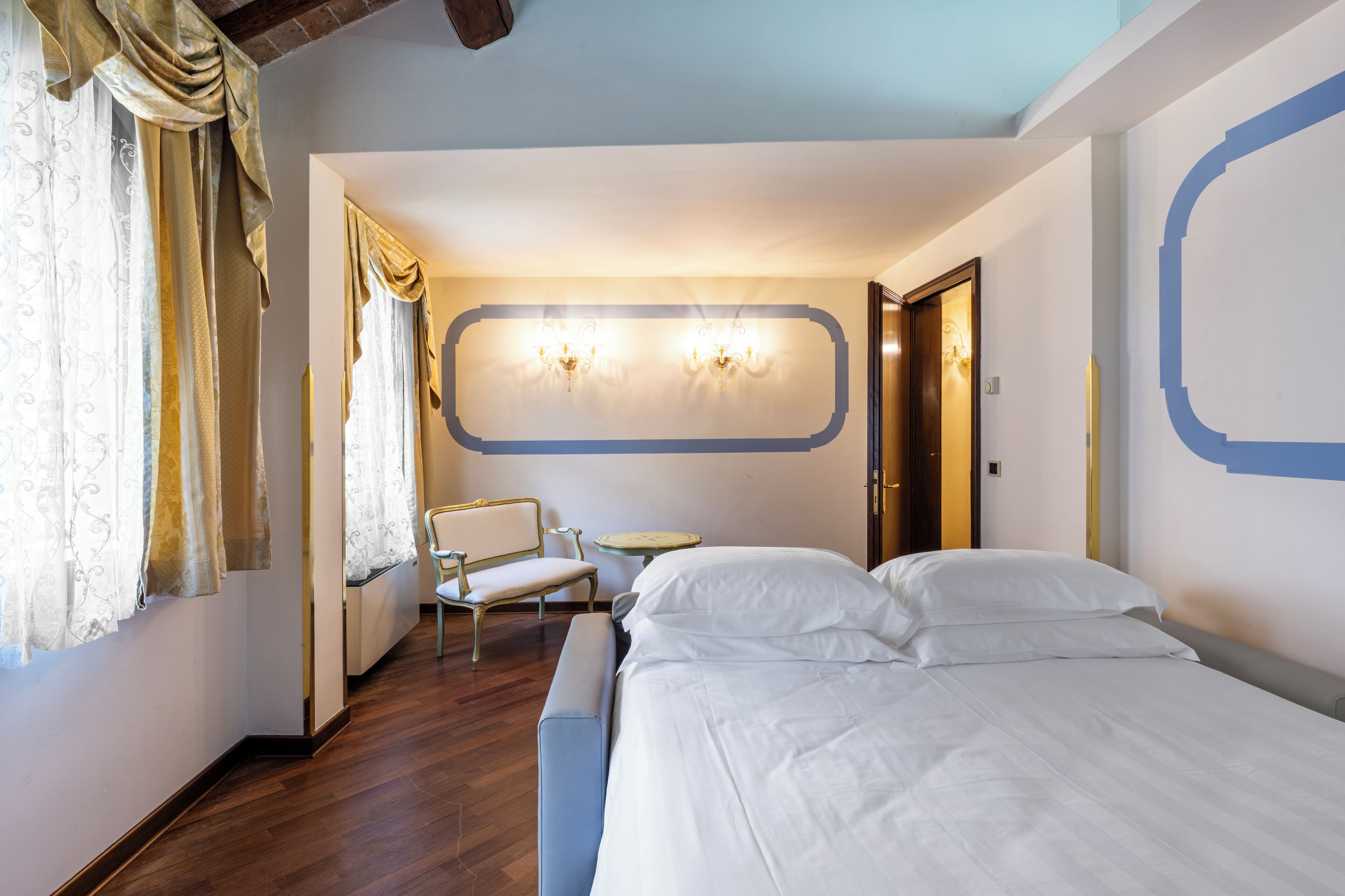 A hotel room with a bed, a chair, a small table, and curtains.