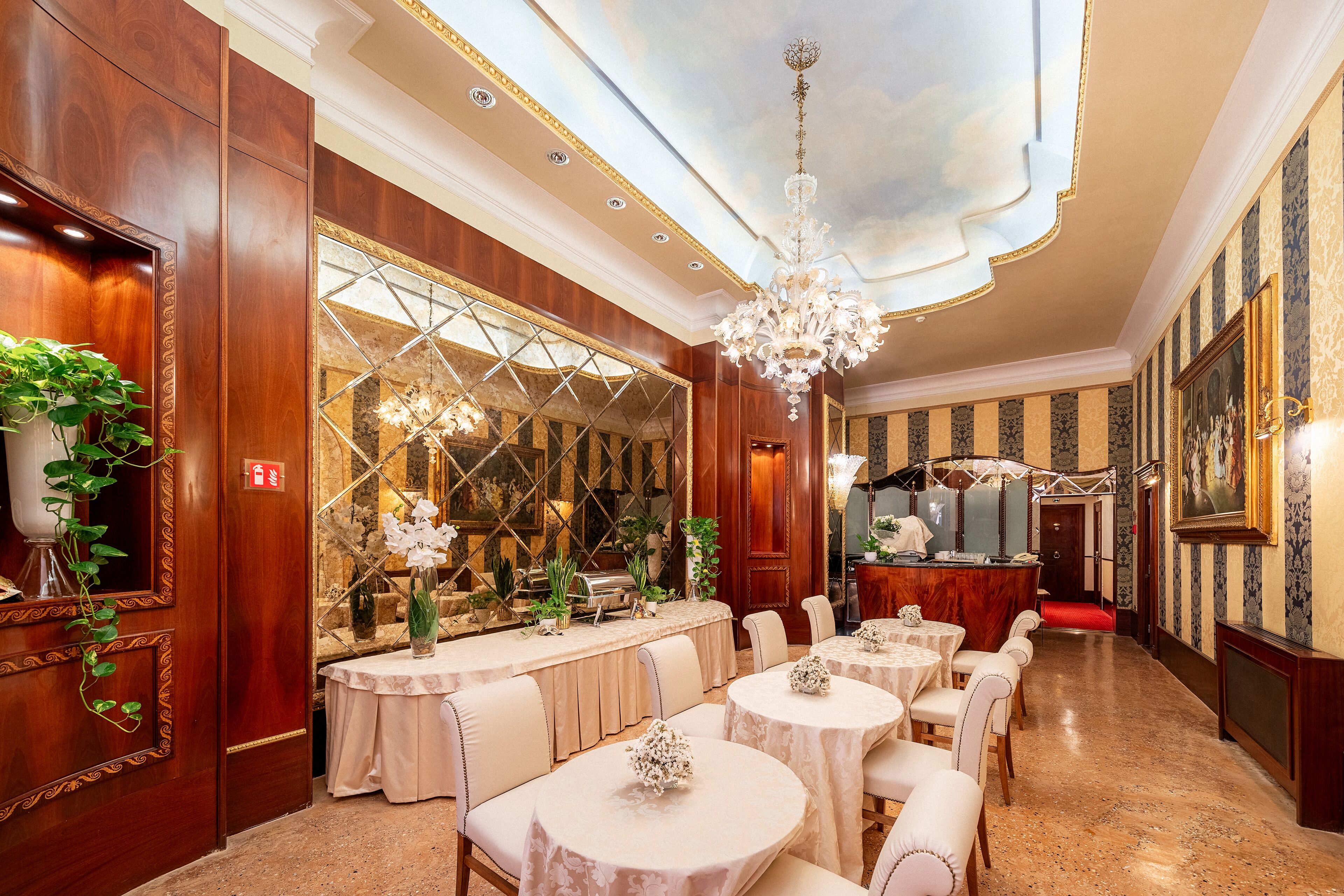 A formal dining area with round tables, white chairs, and a chandelier.