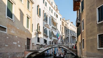 A canal with a bridge, buildings with balconies, and flags.