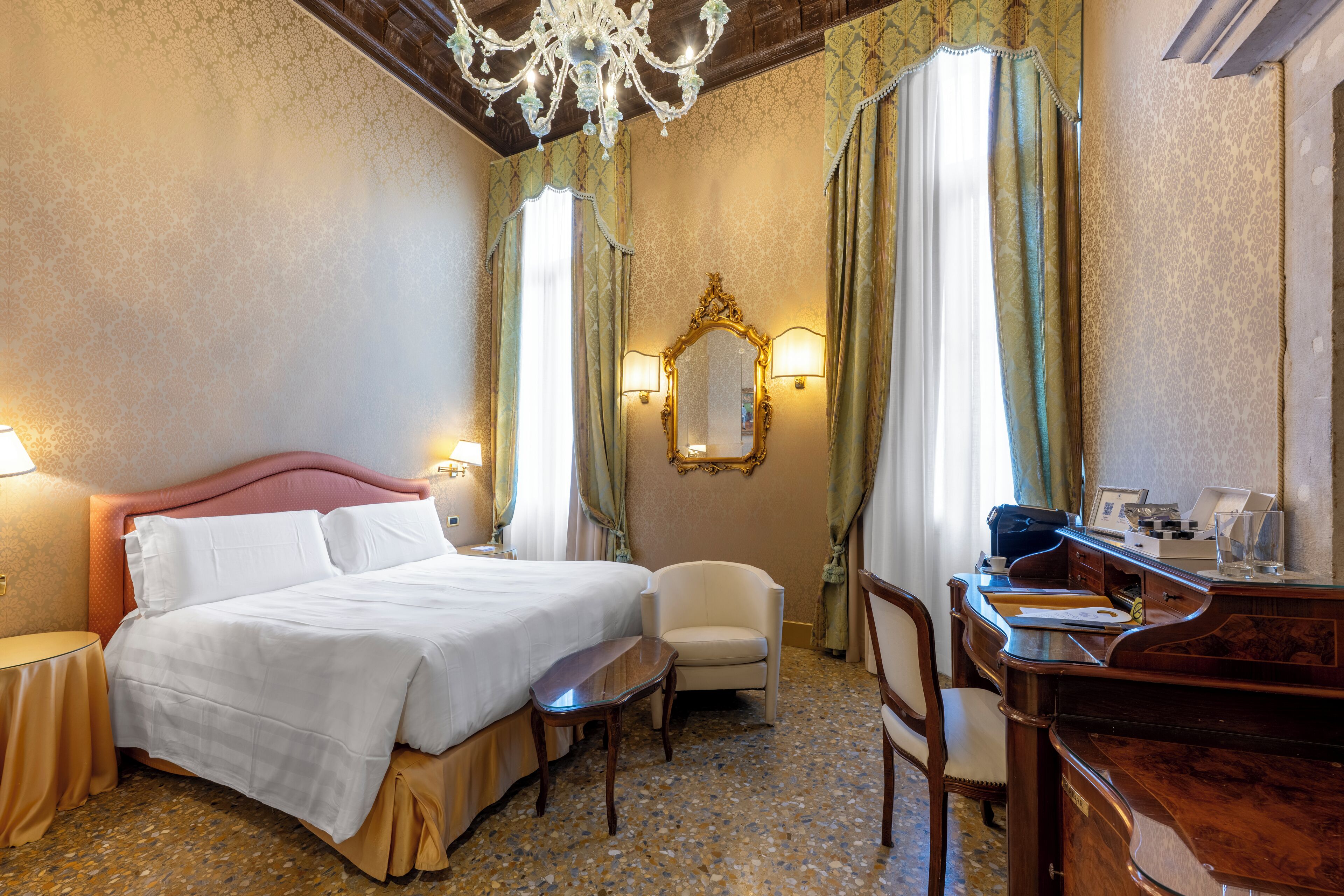 Quarto de hotel com uma cama grande, uma escrivaninha, uma cadeira e um espelho.