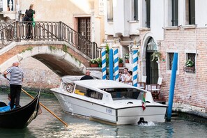 Una escena con un canal, un barco, un puente y edificios con balcones.