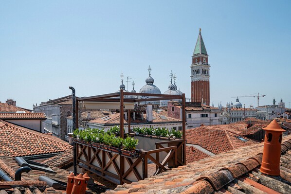 Una terraza en la azotea con tejas de terracota, una pérgola de madera y plantas en macetas.