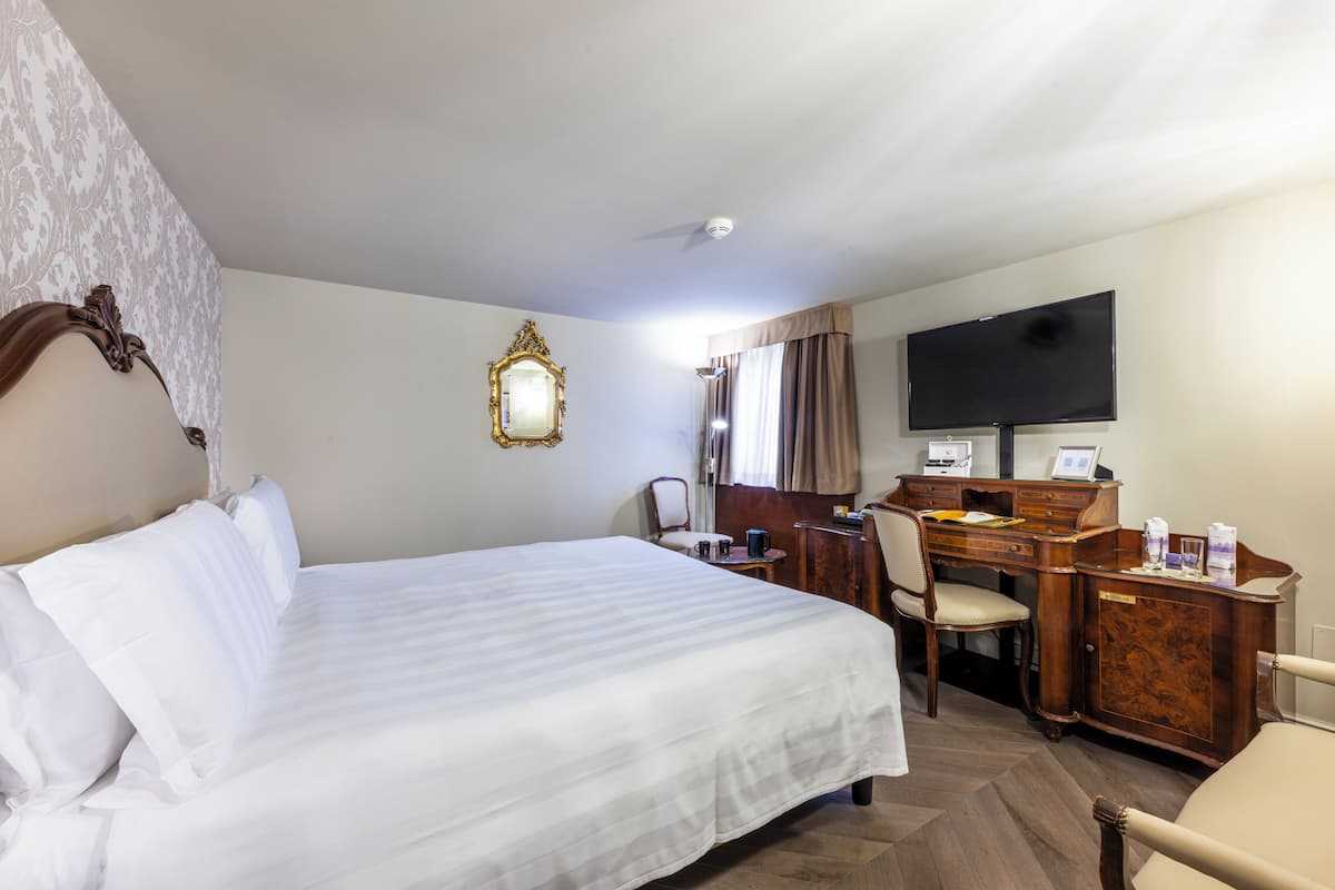 A hotel room with a large bed, a desk with a computer, a television, and a mirror.