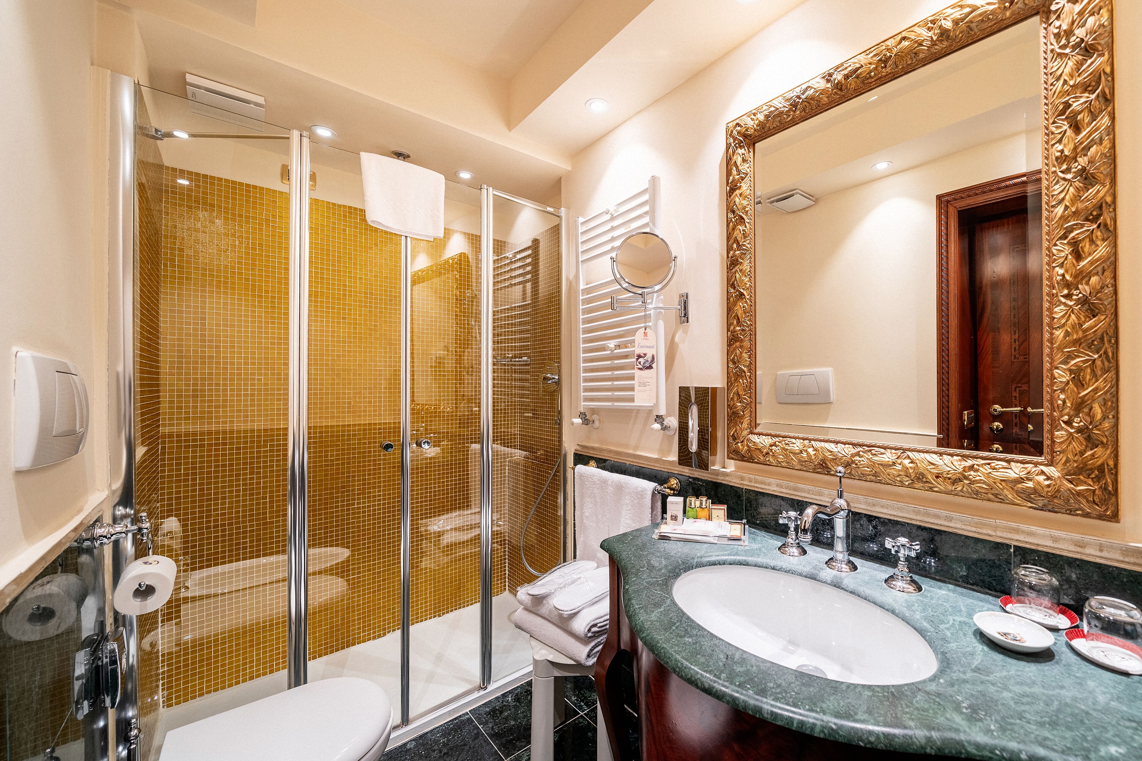 A bathroom with a glass-enclosed shower, a sink with a marble countertop, and a large ornate mirror.