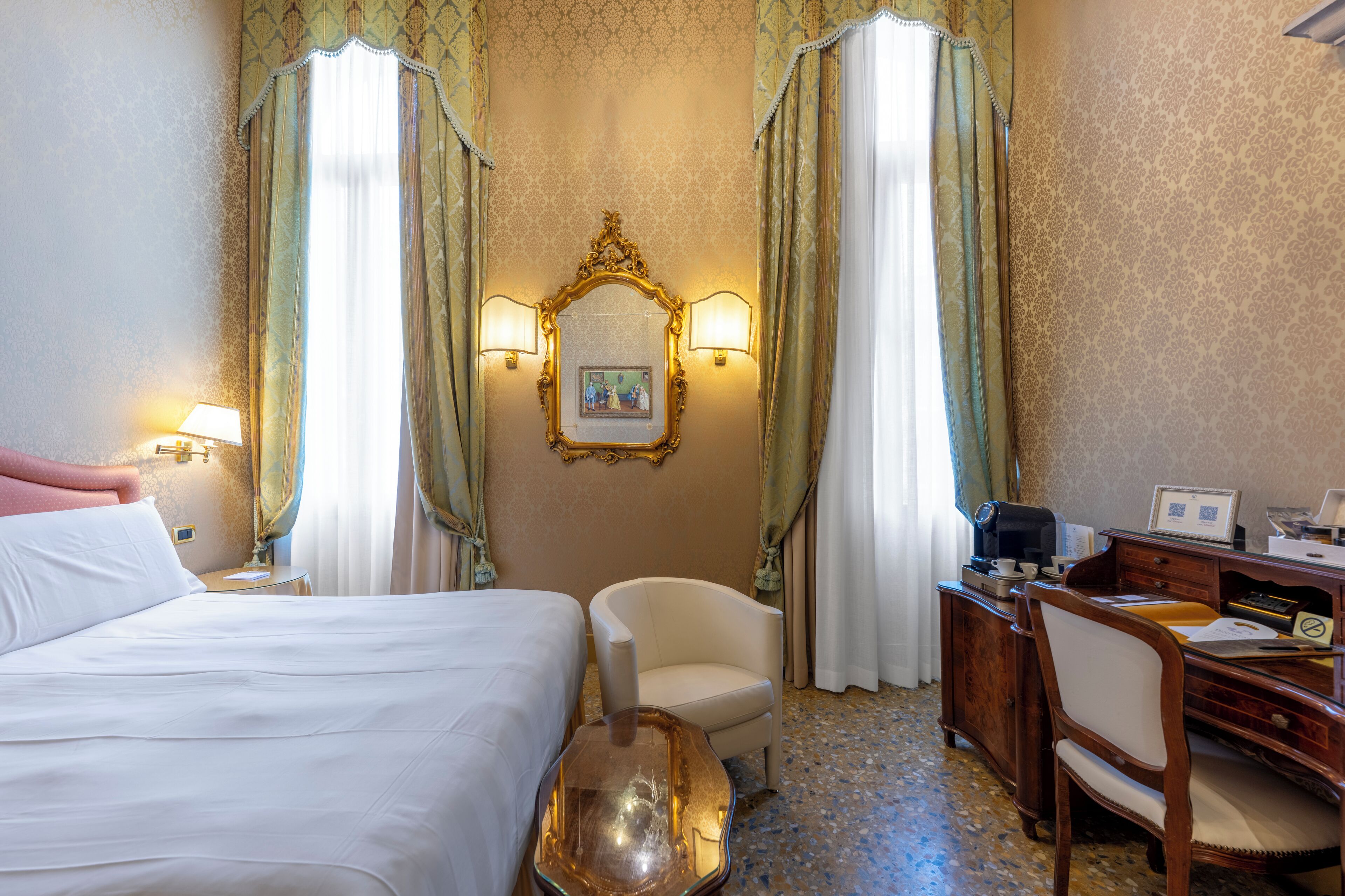 A hotel room with a bed, two chairs, a desk, and a mirror.