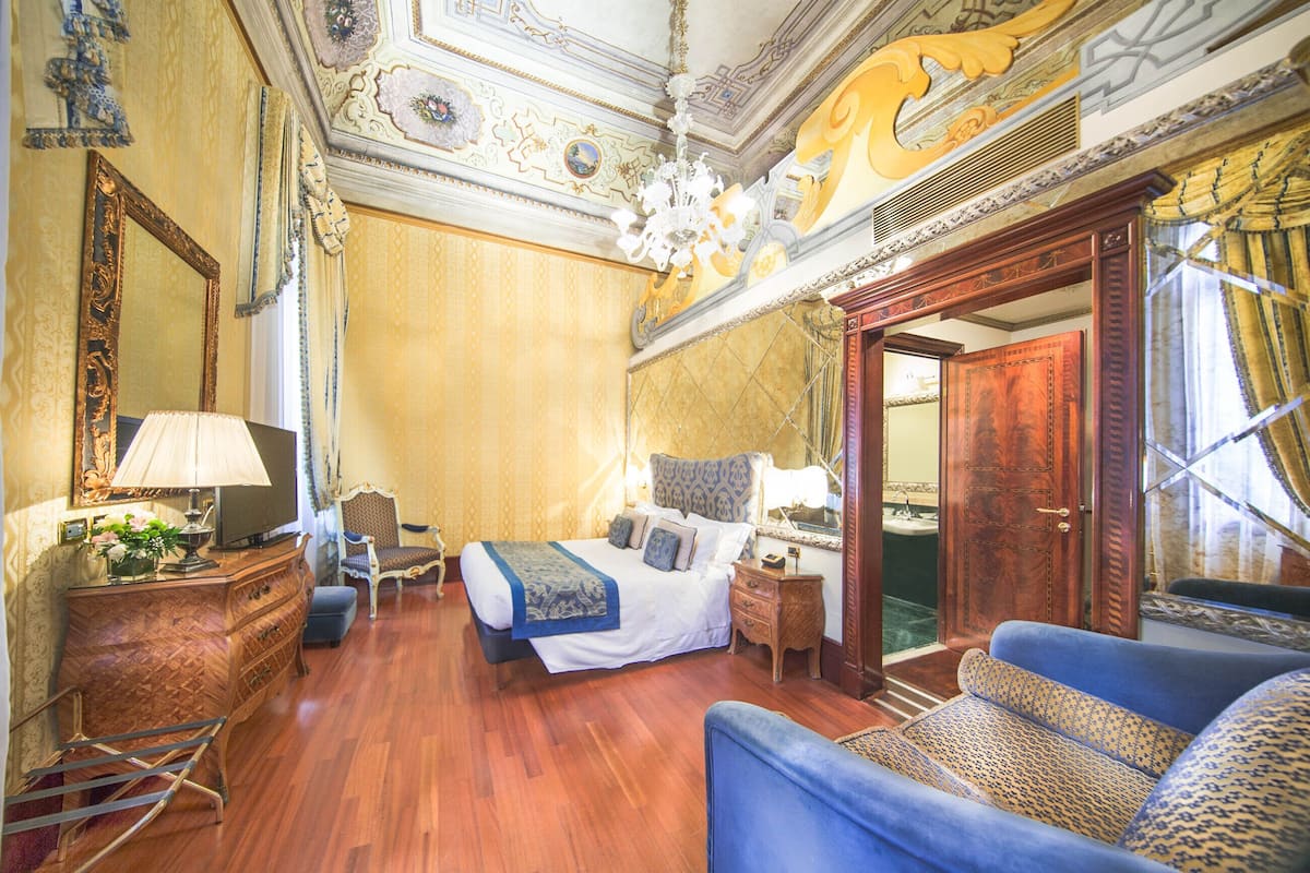 A spacious bedroom with a large bed, a sitting area with a sofa, a dresser, and a television.