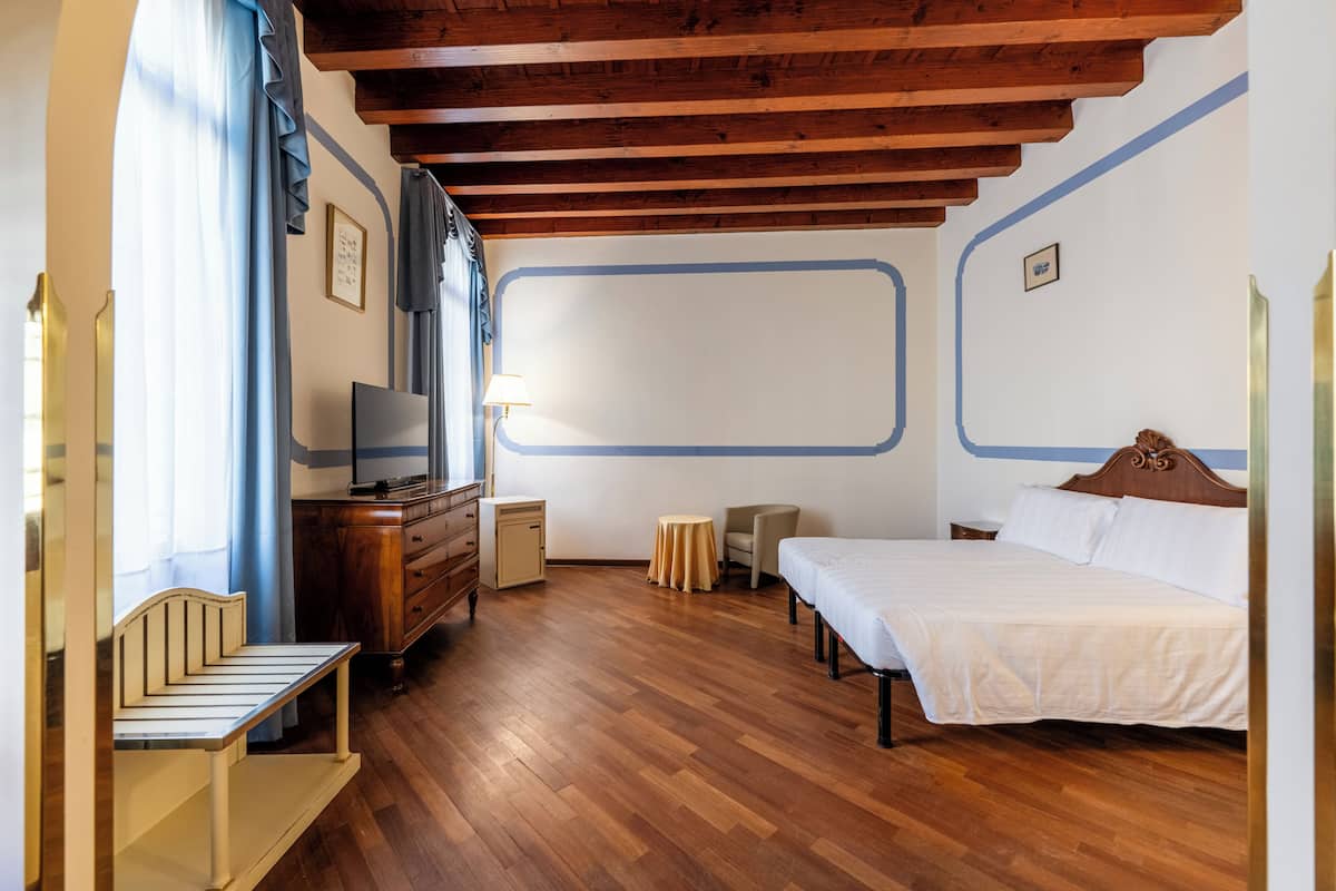 A hotel room with a wooden ceiling, a bed, a TV, a desk, and a chair.