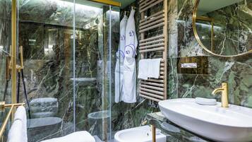 Une salle de bain moderne avec une douche à parois de verre, un mur en marbre, un lavabo blanc avec un robinet doré et un porte-serviettes.