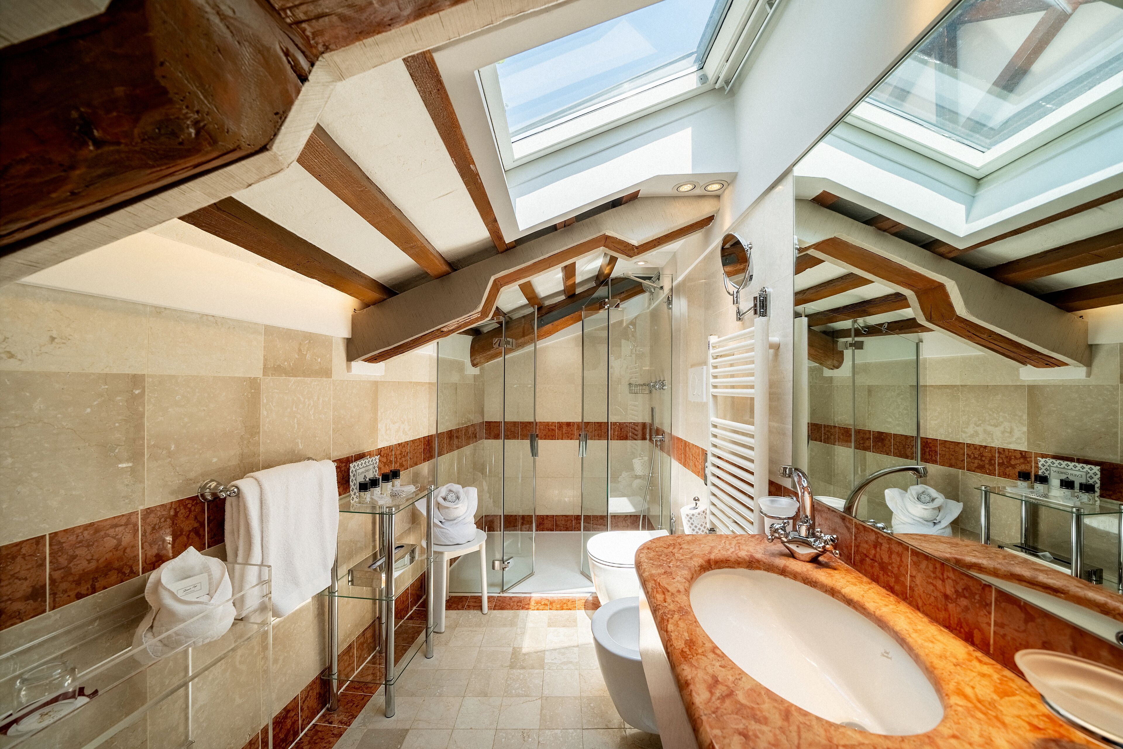 A modern bathroom with a skylight, a glass shower enclosure, and a marble-tiled floor.