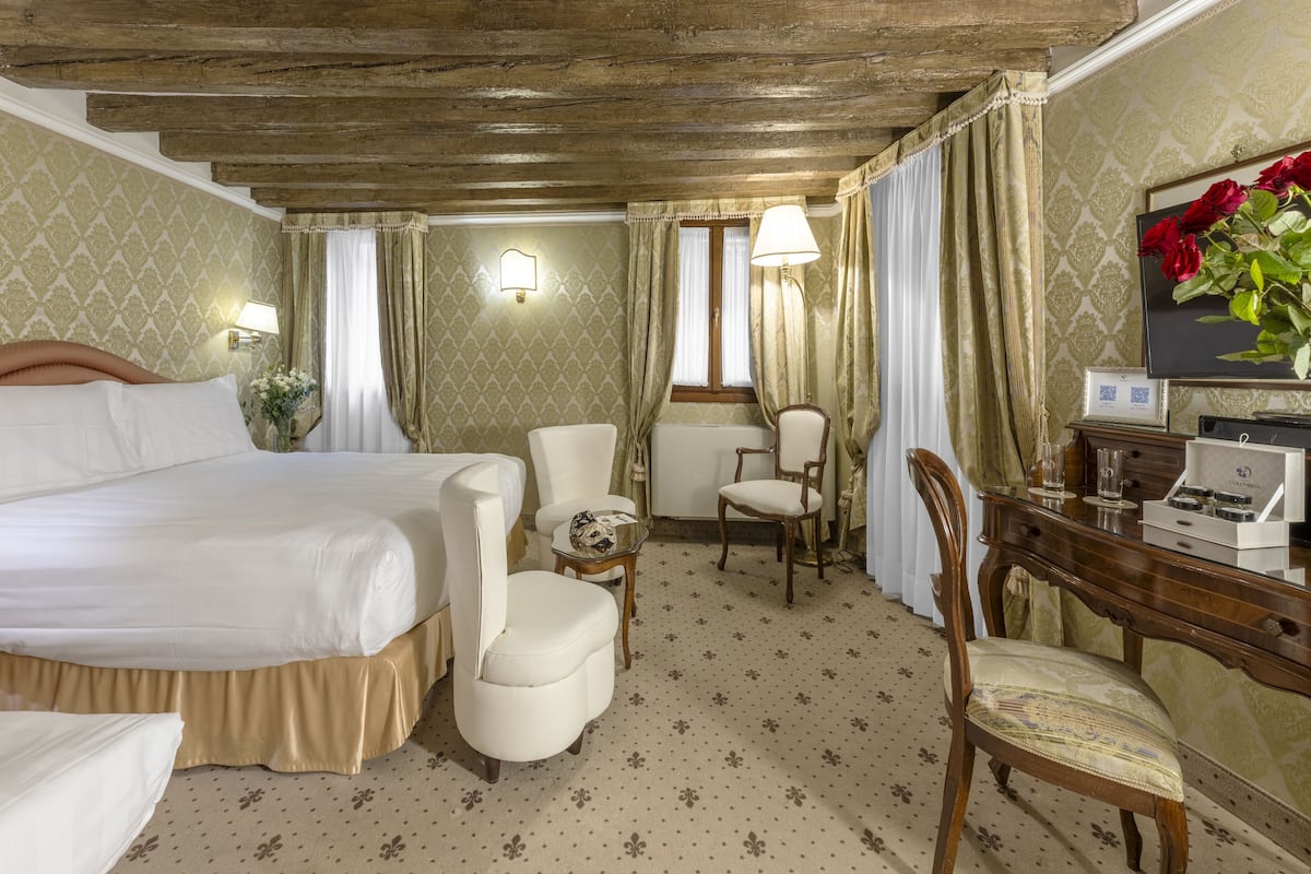 A hotel room with a large bed, two chairs, a small table, a desk with a computer, and a window with curtains.