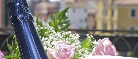 Una botella de champán con un adorno decorativo, rodeada de rosas rosadas y flores de espino.