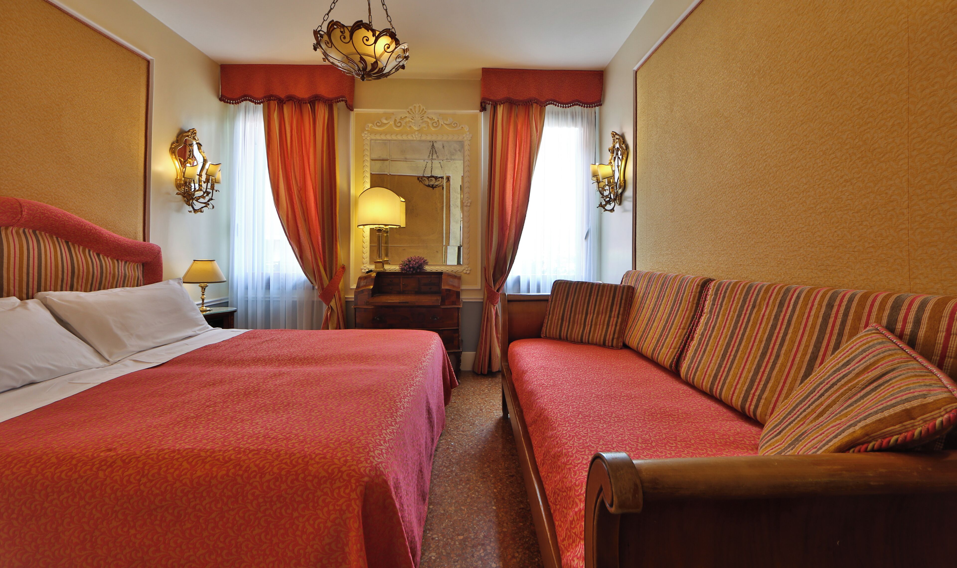 A hotel room with two beds, a sofa, a dresser, and a mirror.