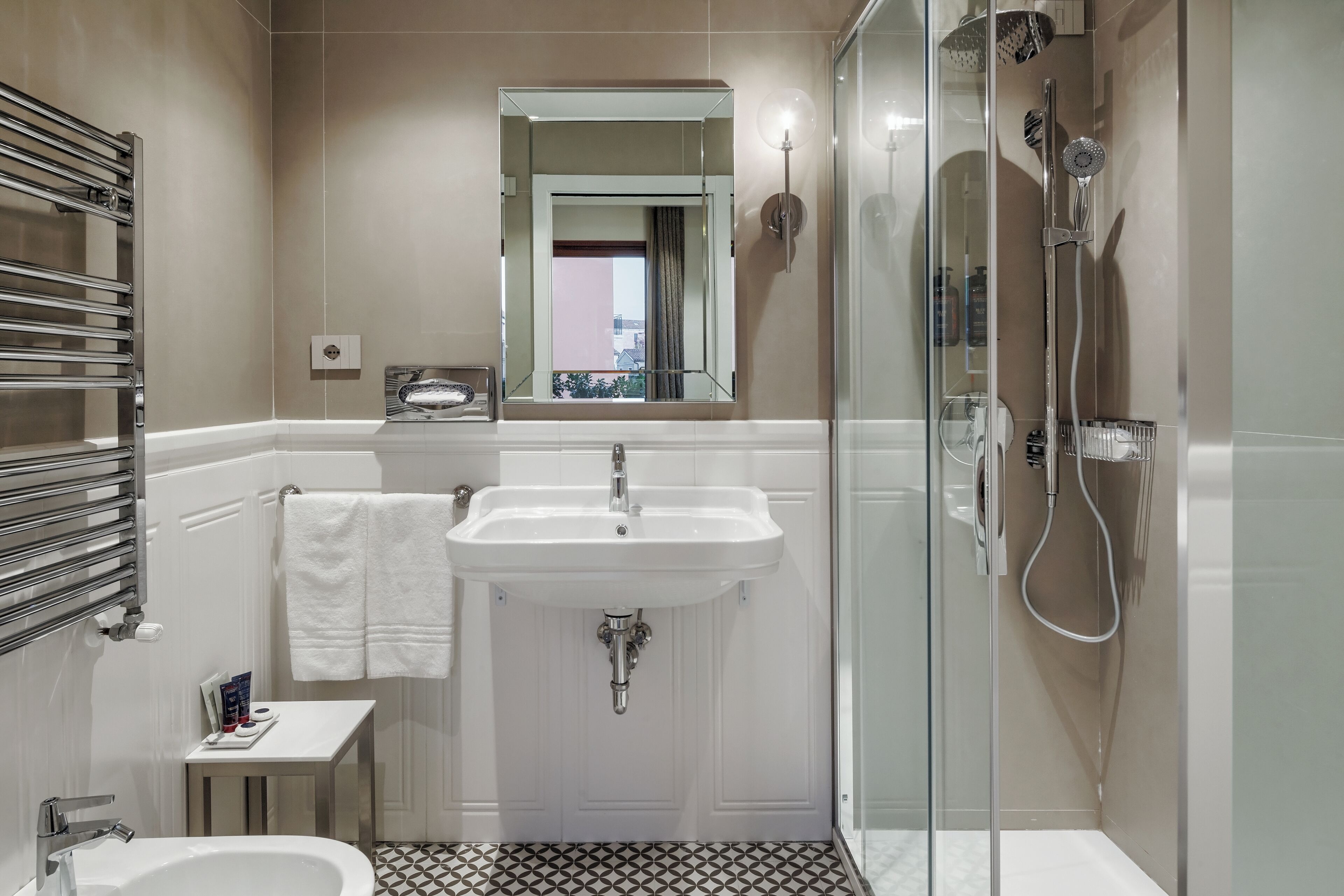 A modern bathroom with a glass-enclosed shower, a double sink, and a small vanity with a towel rack.
