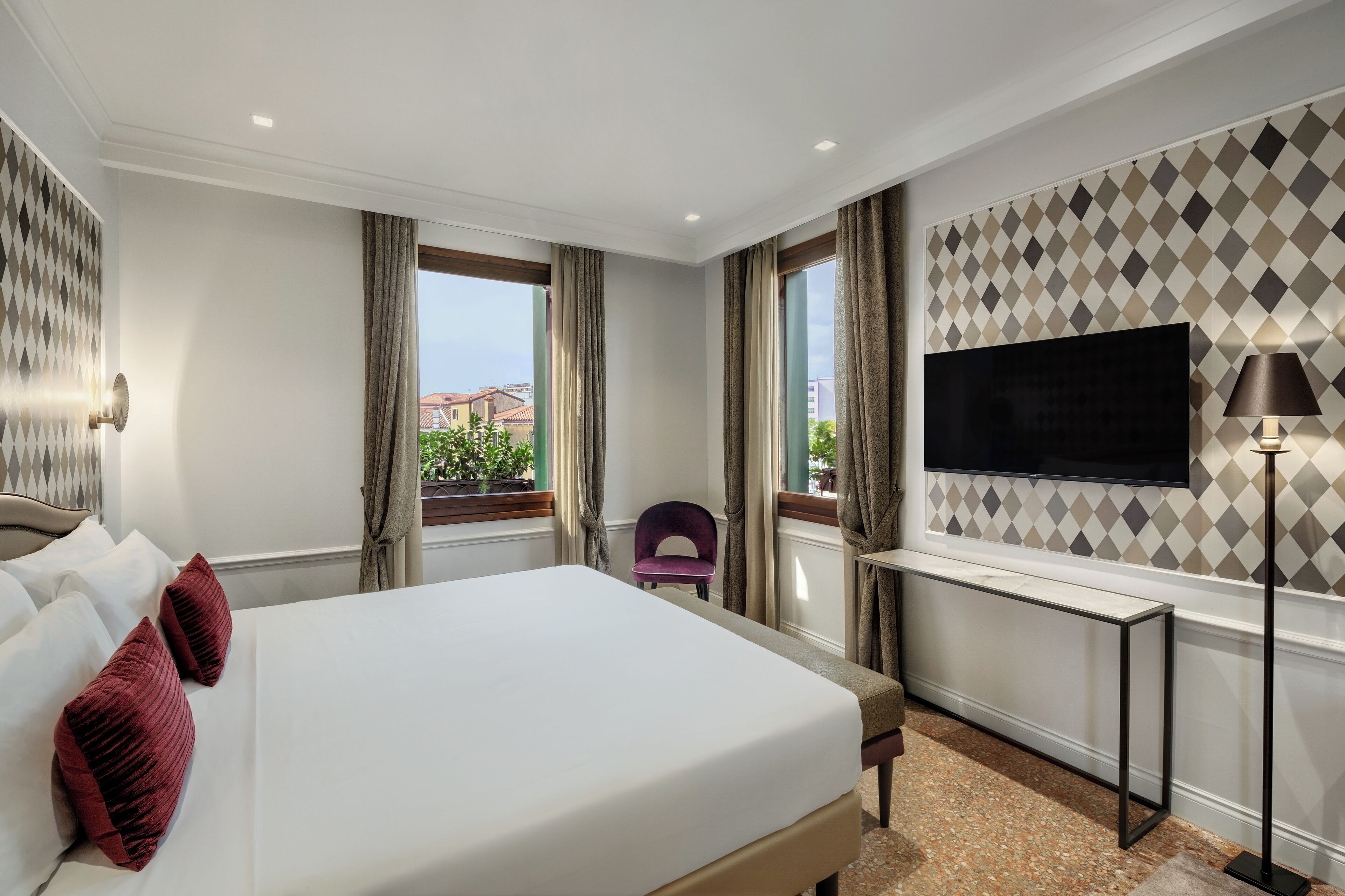 Une chambre d’hôtel avec un grand lit, un bureau, une chaise, une télévision et une fenêtre avec des rideaux.