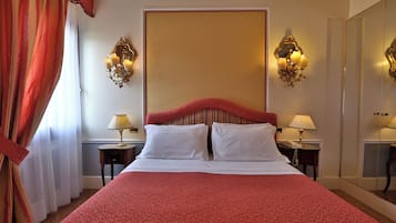 Habitación de hotel con una cama grande, dos mesitas de noche con lámparas, un espejo amplio y una cortina roja.