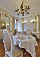 Comedor formal con candelabro, espejos ornamentados y una mesa blanca dispuesta para una comida.