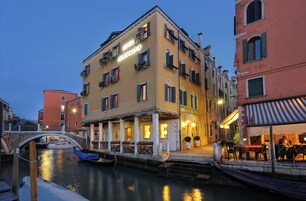 Un hotel con balcón que da a un canal, un puente y otros edificios.