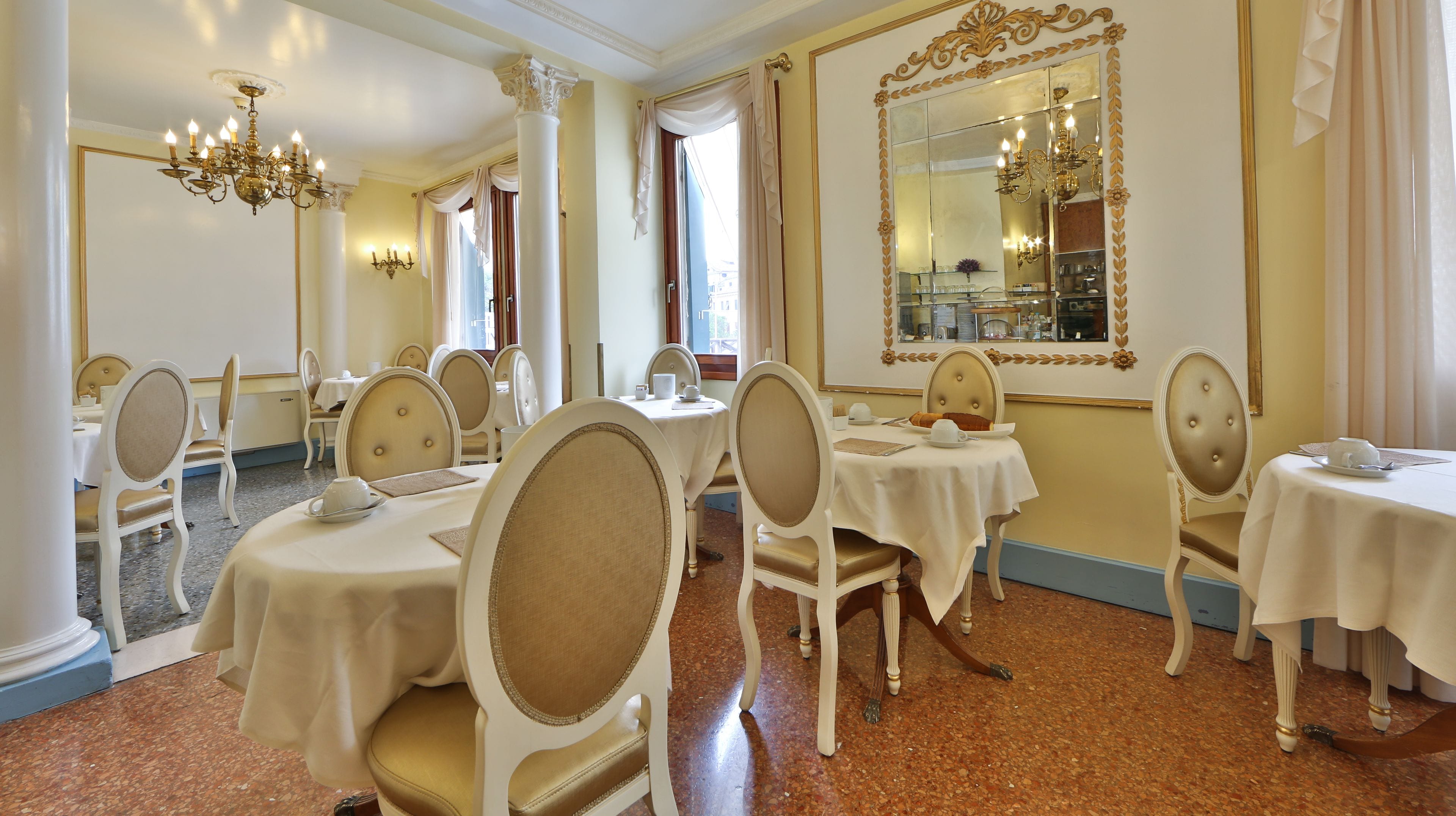 Uma sala de jantar com mesas e cadeiras redondas, lustres e um espelho grande.