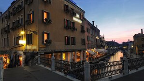 Un edificio histórico con varios balcones, un letrero que indica un restaurante y un canal al fondo.