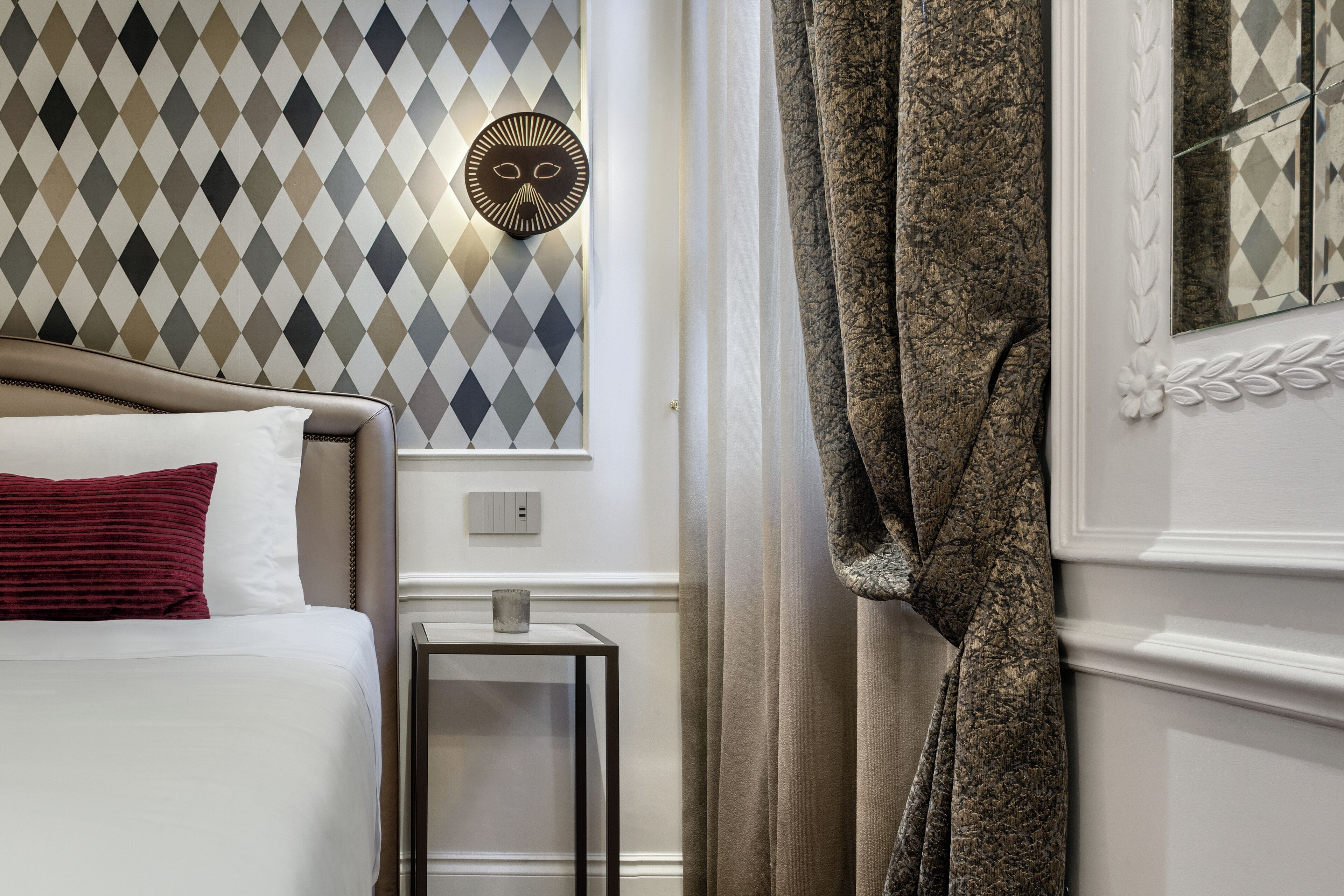Habitación de hotel con cama, mesita de noche, lámpara de pared y cortina.