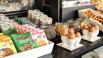 Un tavolo da buffet con diversi cibi, tra cui scatole di cereali, vasetti di creme e uova in tazzine.