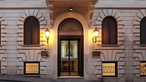 A building facade with a central entrance, flanked by two arched windows with shutters, and two smaller windows with decorative iron grilles. - Hotel Barberini (Rome)