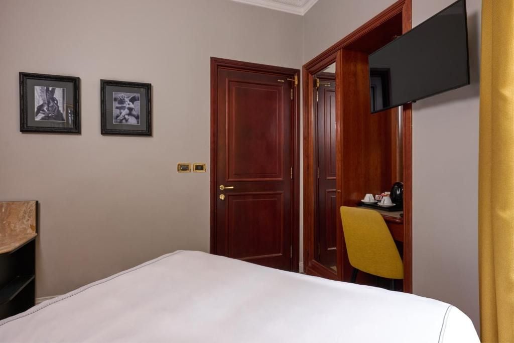 Una camera d'albergo con un letto, una scrivania, una sedia, una televisione e due quadri appesi al muro.