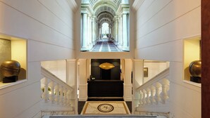 A grand hallway with a marble floor, a central chandelier, and a view to the upper floor. - Hotel Barberini (Rome)