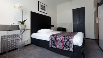 Una habitación de hotel moderna con una cama, un escritorio de vidrio, una silla, una planta en maceta y una puerta.