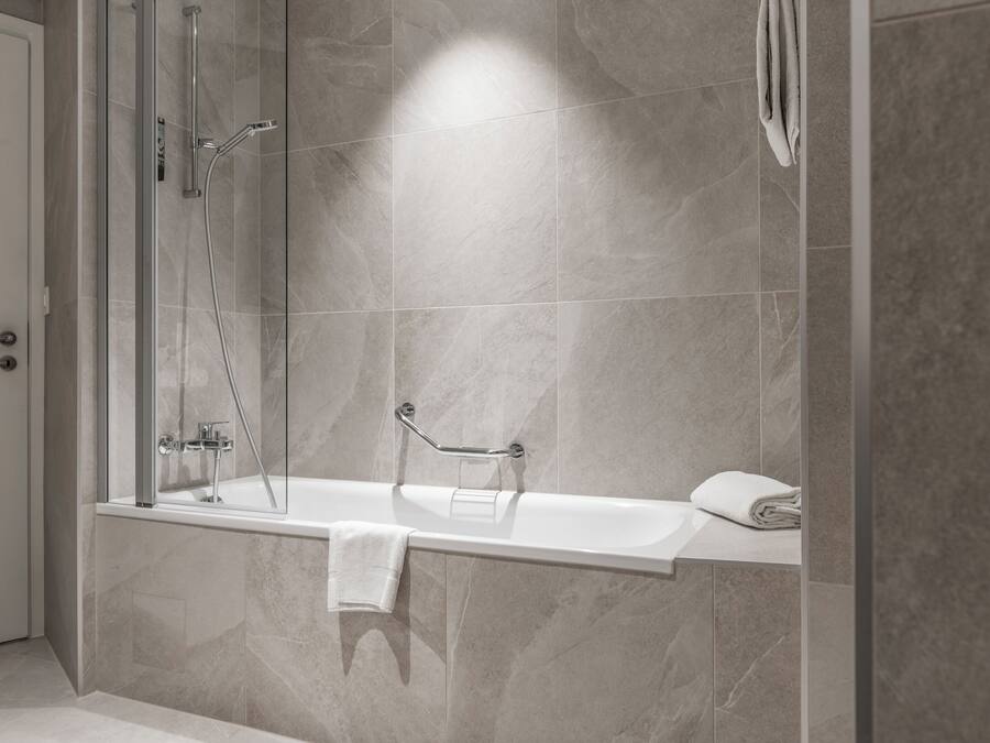 A modern bathroom with a glass-enclosed shower, a white bathtub, and a towel rack.