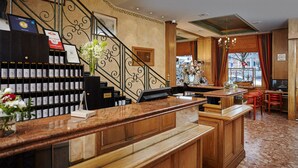 A hotel reception area with a wooden reception desk, a mail slot, a staircase, and a view of the street outside. - Hotel Suisse (Geneva)